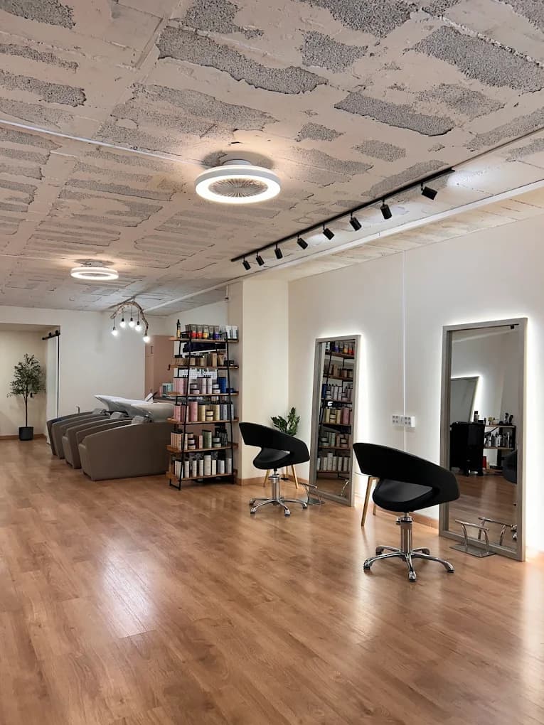 Peluquería Ana Gago Hairsalon en el Eixample, Barcelona Interior de Ana Gago Hairsalon, peluquería en Carrer de Diputació 410, Eixample de Barcelona — puestos de peluquería, espejos retroiluminados y estantería de productos Nashi Argan